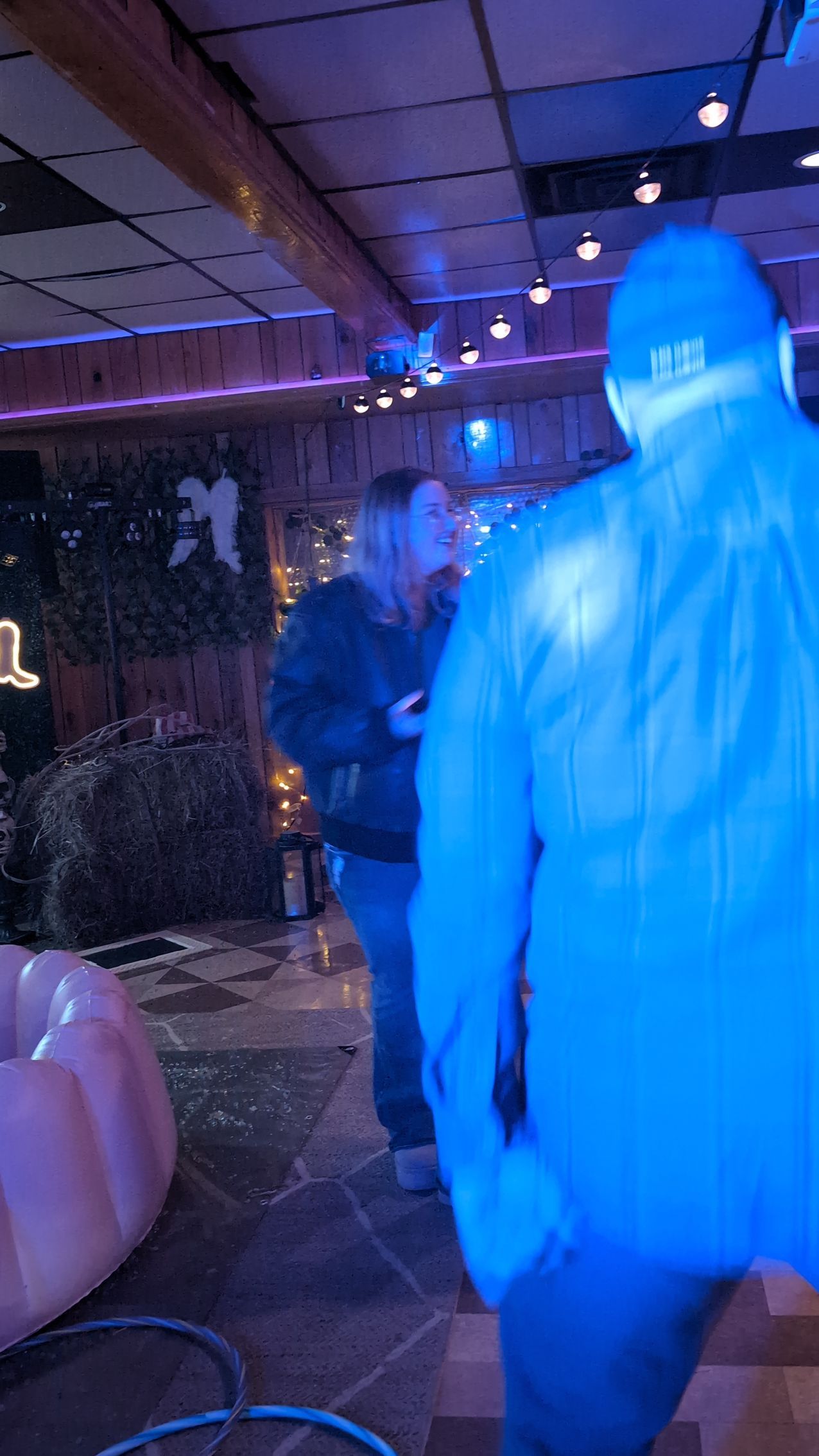 People dancing in a dim nightclub with blue lighting and hanging string lights