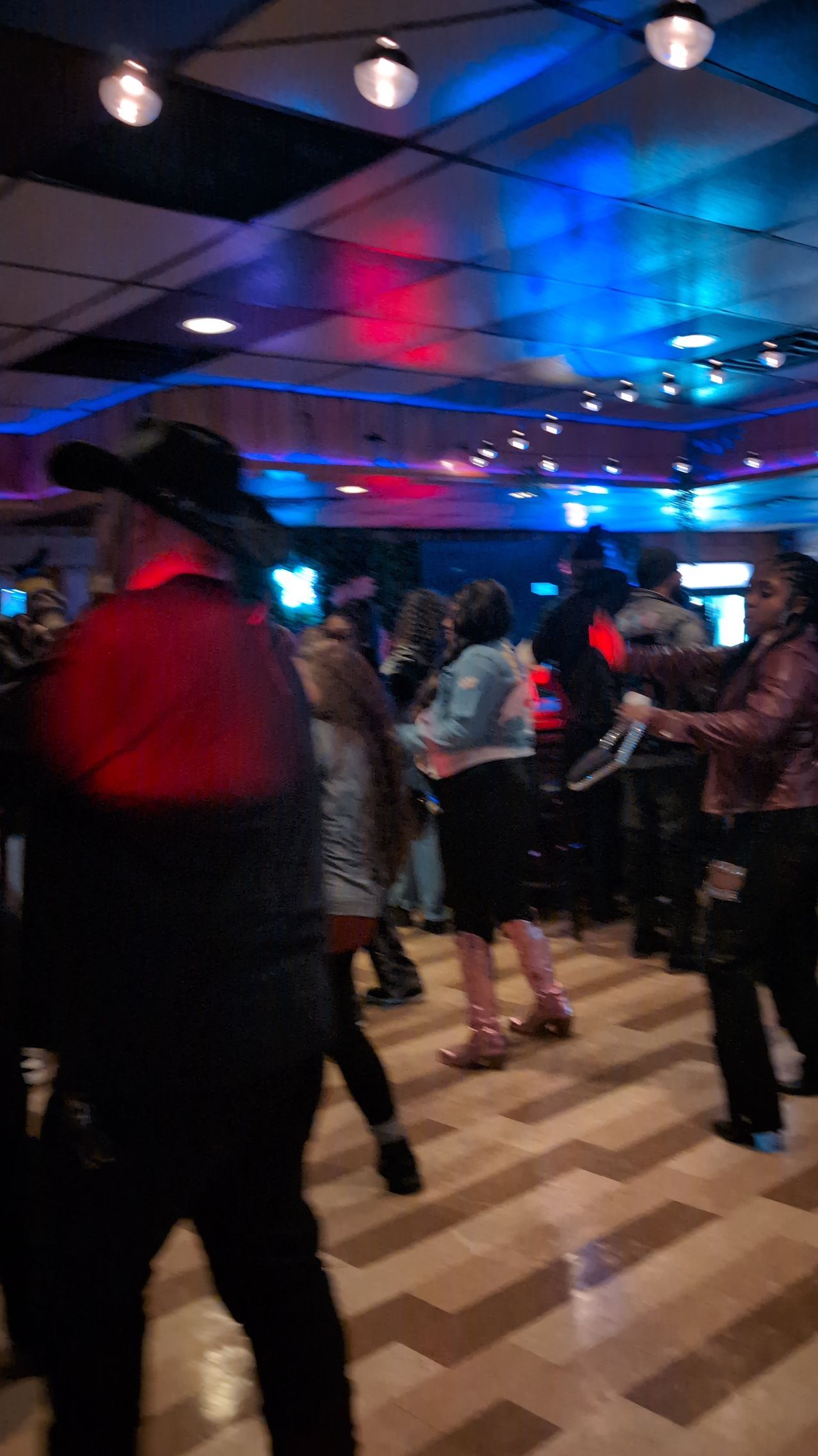 People dancing in a dim club with blue and red lights and a wood floor