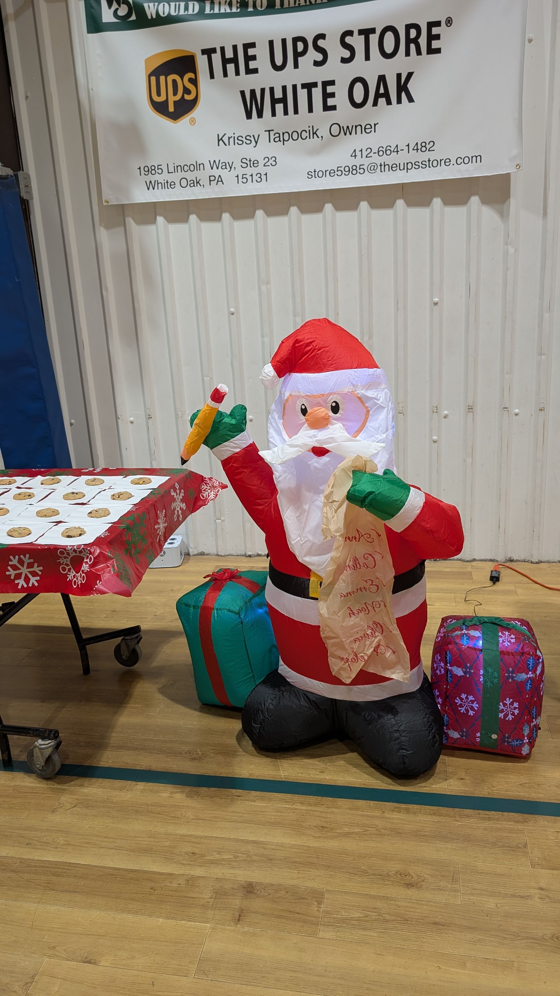 Inflatable Santa seated by wrapped gifts inside The UPS Store White Oak lobby