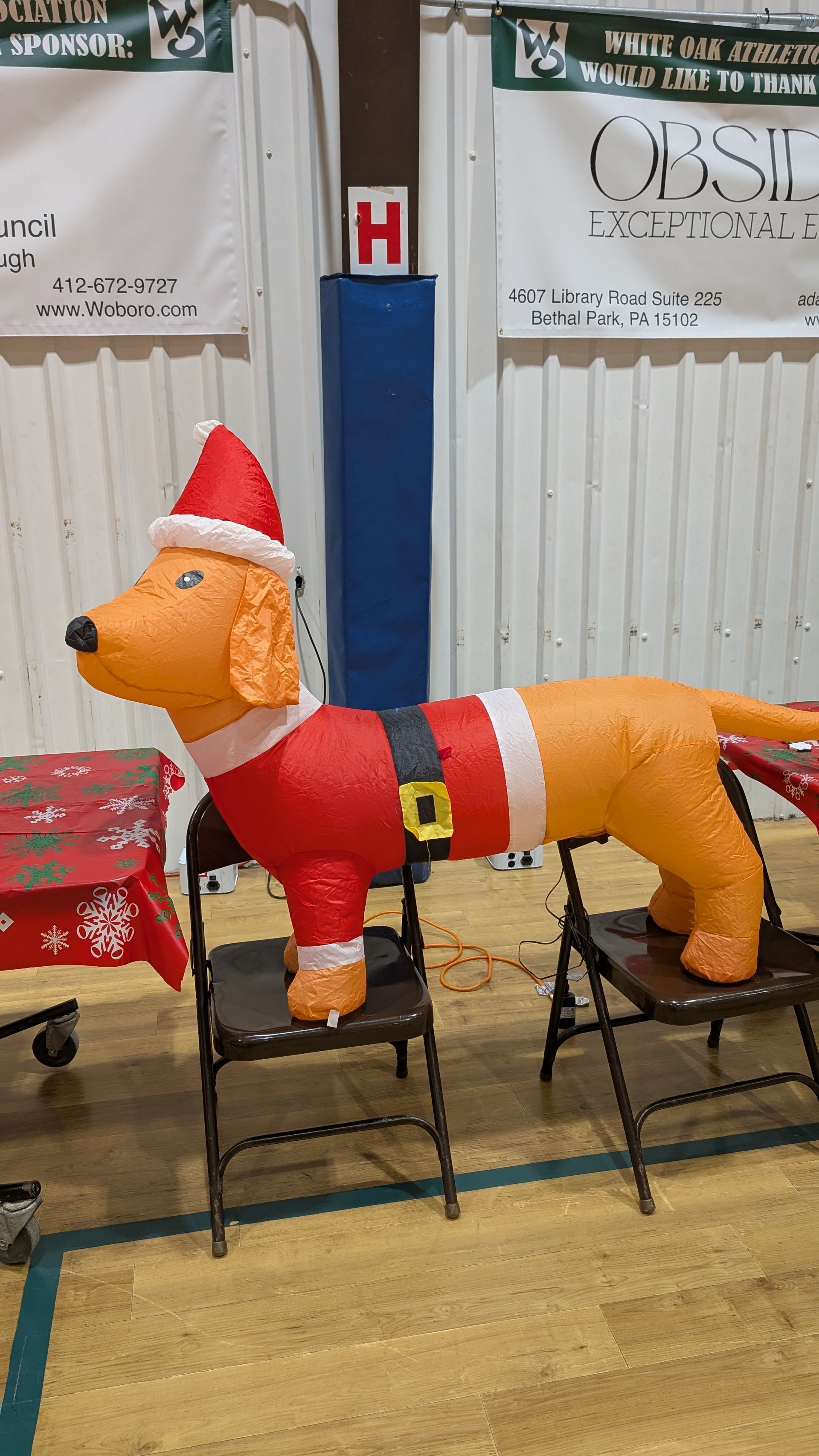 Inflatable fox in a Santa suit standing indoors in front of a wall and chairs