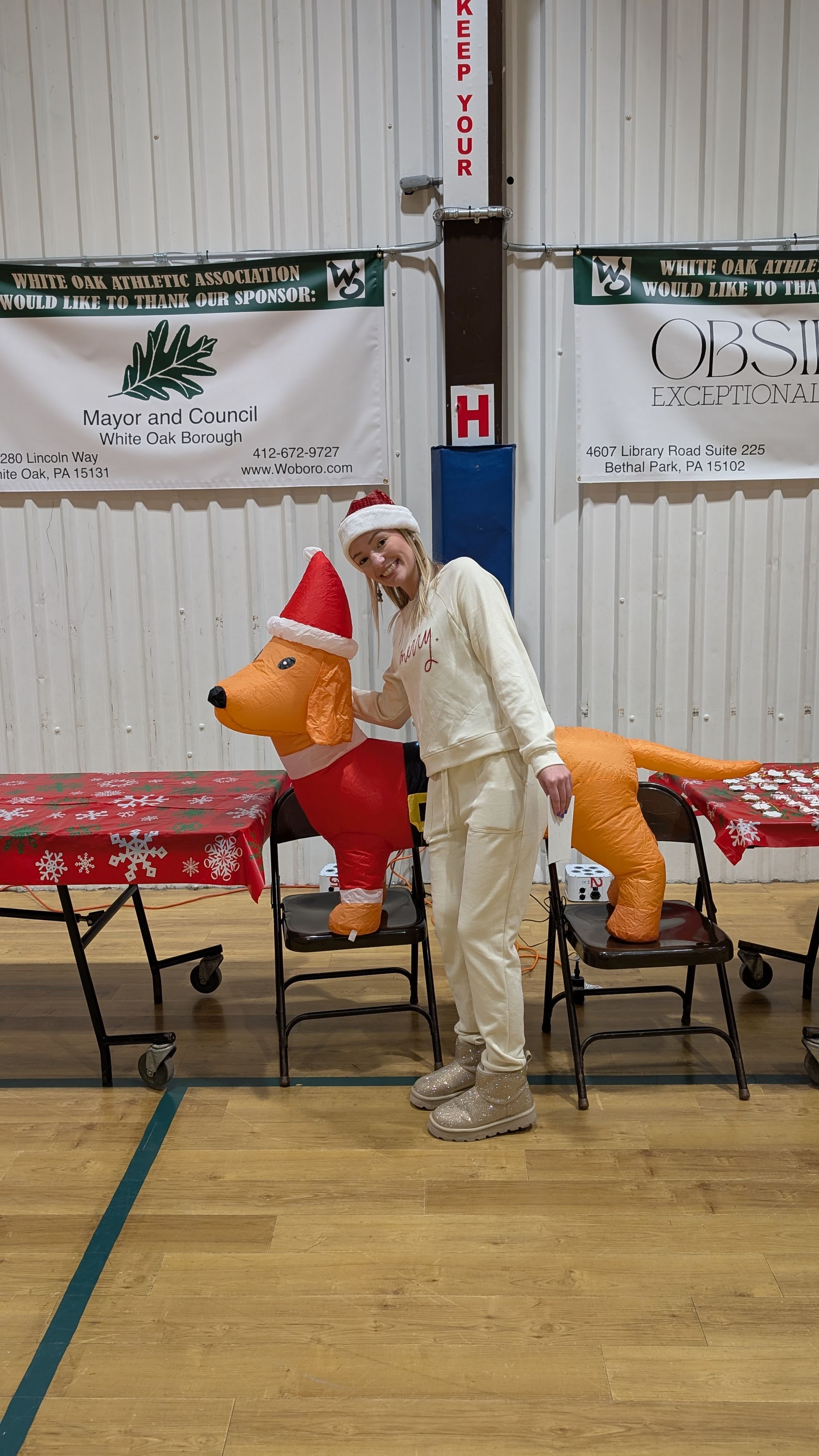 Person in a Santa hat standing beside an orange inflatable reindeer in a gymnasium.