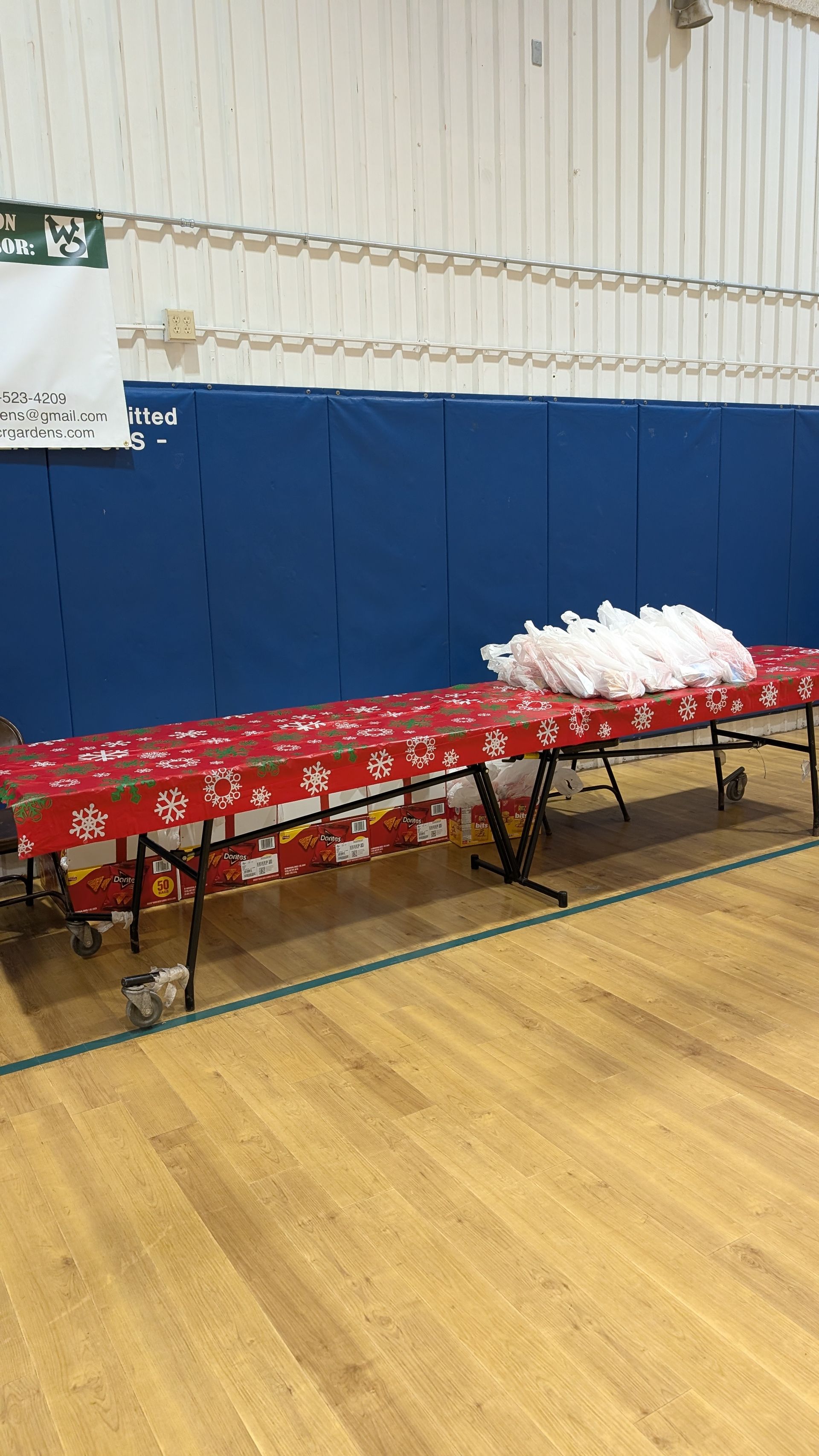 Folded tables with red tablecloths and white bags set up in a gymnasium with blue padded walls.
