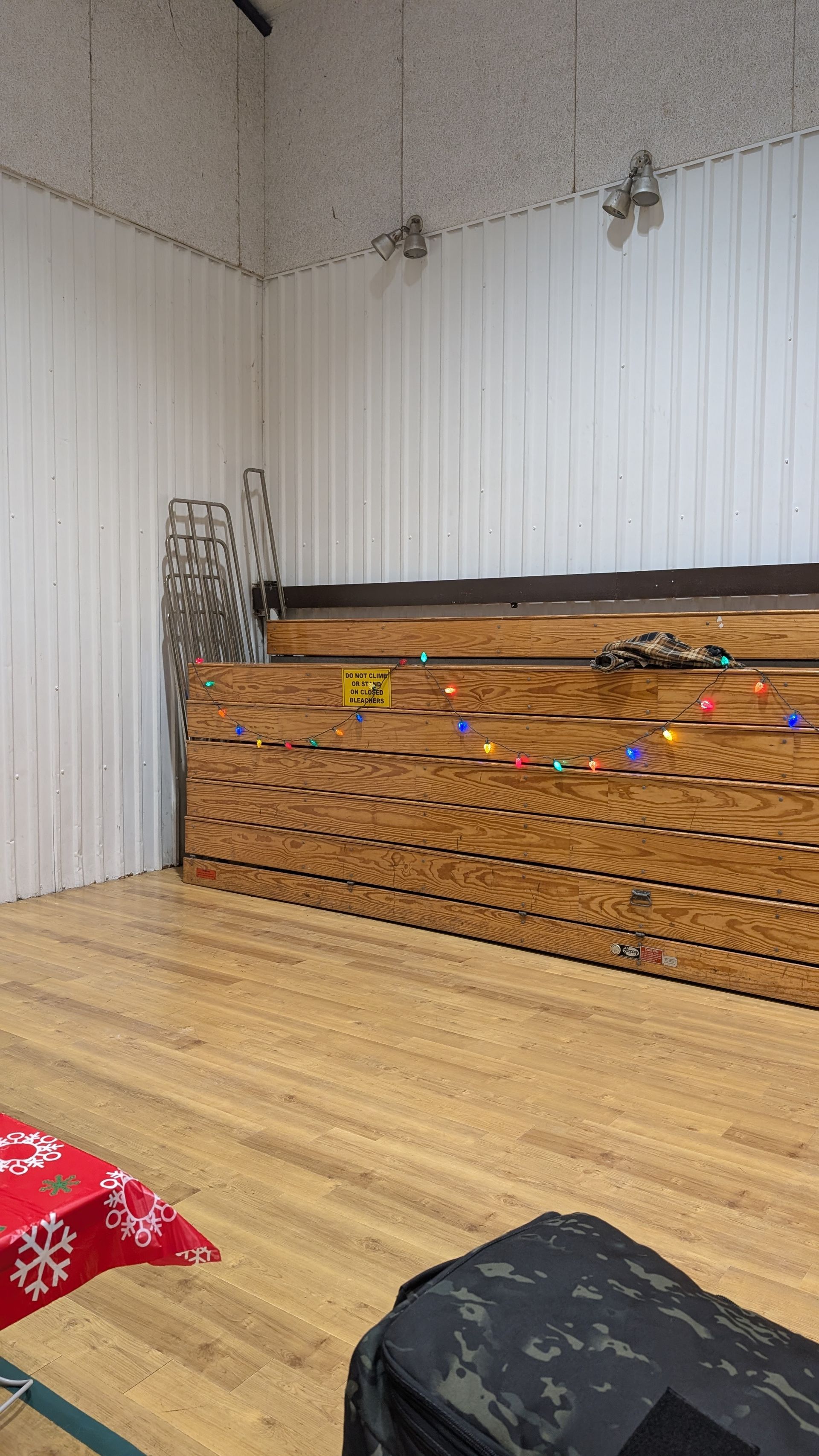 Decorated indoor stage with wooden backdrop, white drapes, colorful string lights, and small stools on a light wood floor
