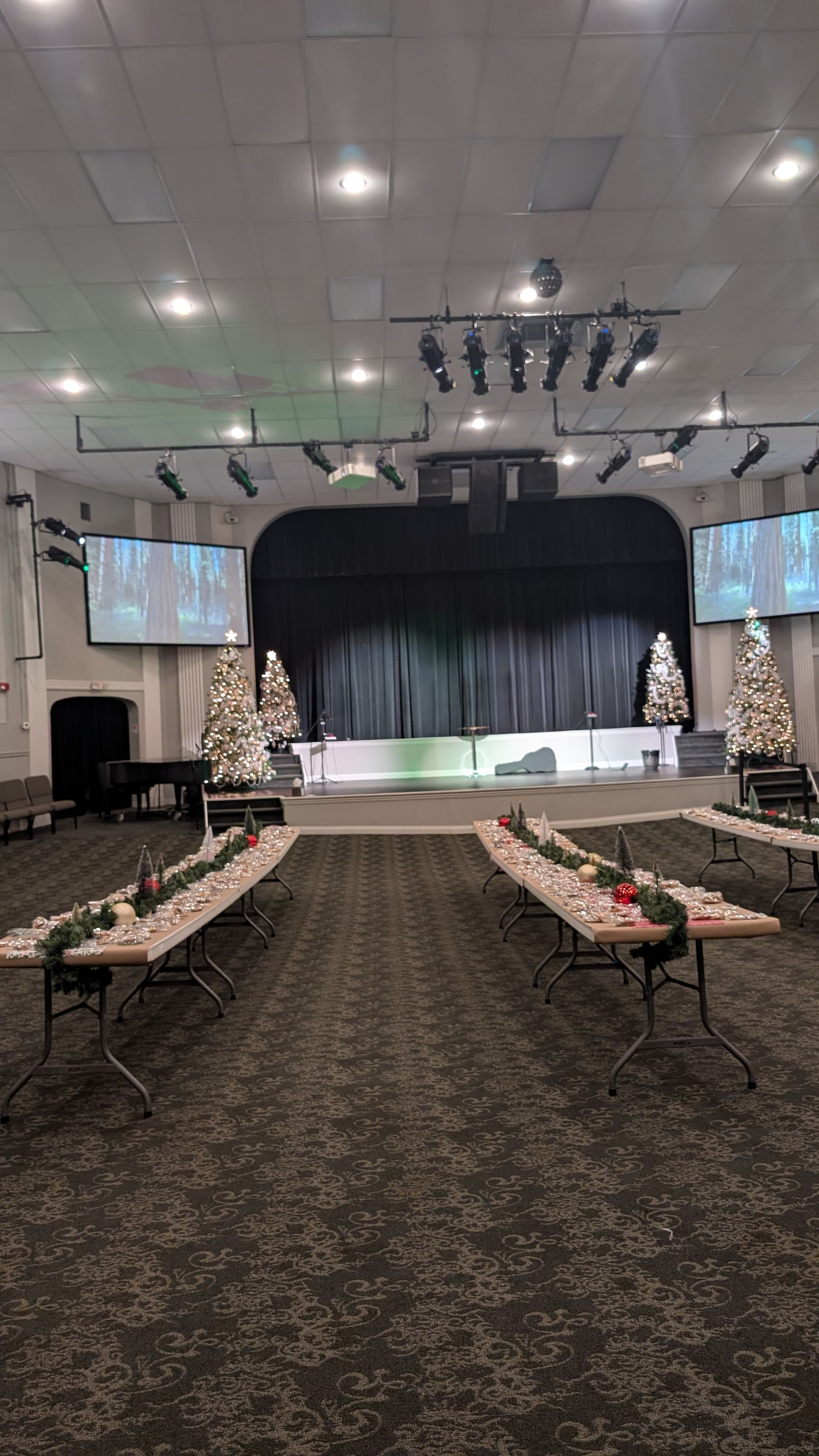 Banquet hall with runway-style aisle, banquet tables, and a lit stage with black drapes at the far end