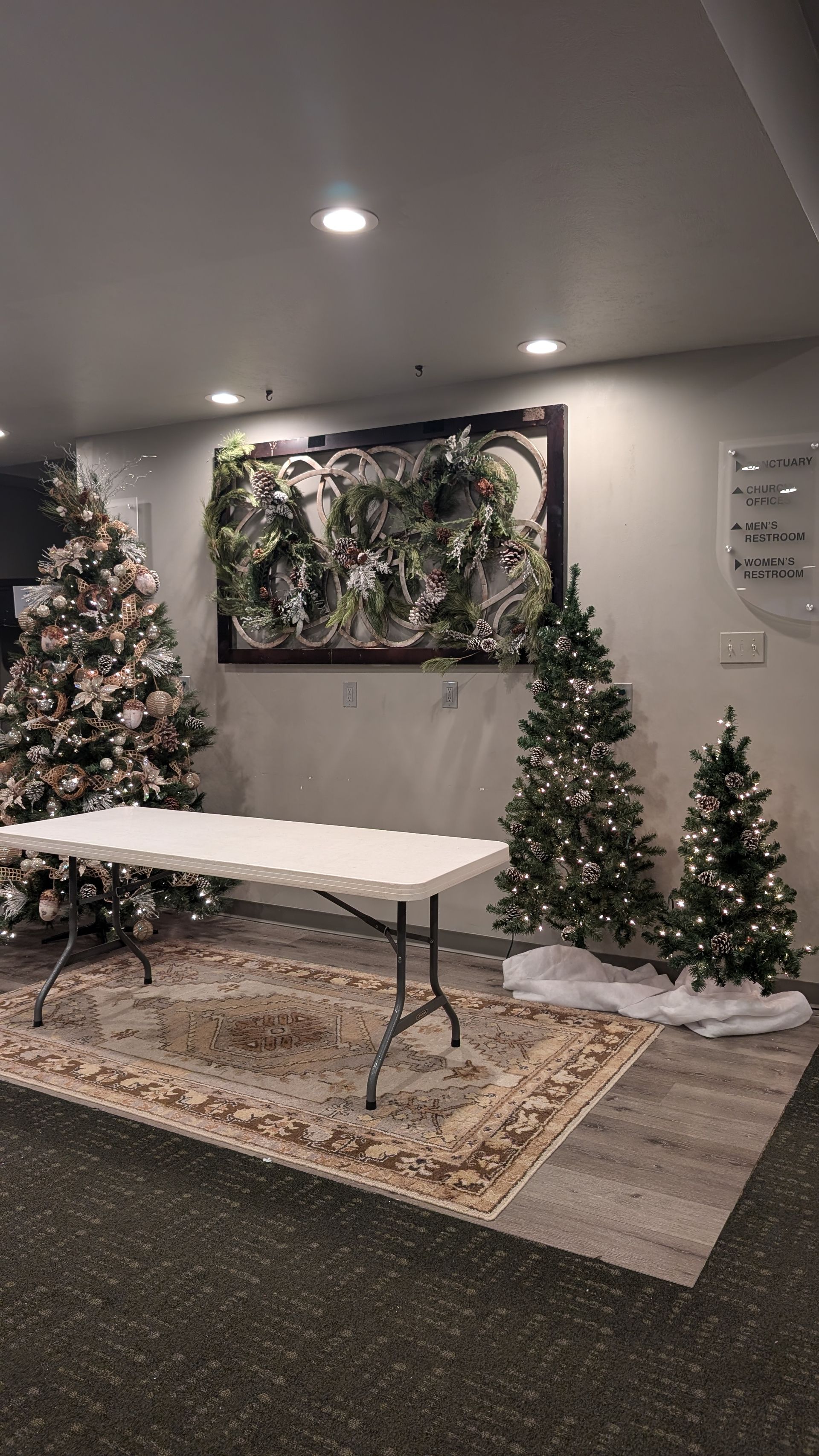 Holiday-decorated room with Christmas trees, a long table, and a floral wall painting.