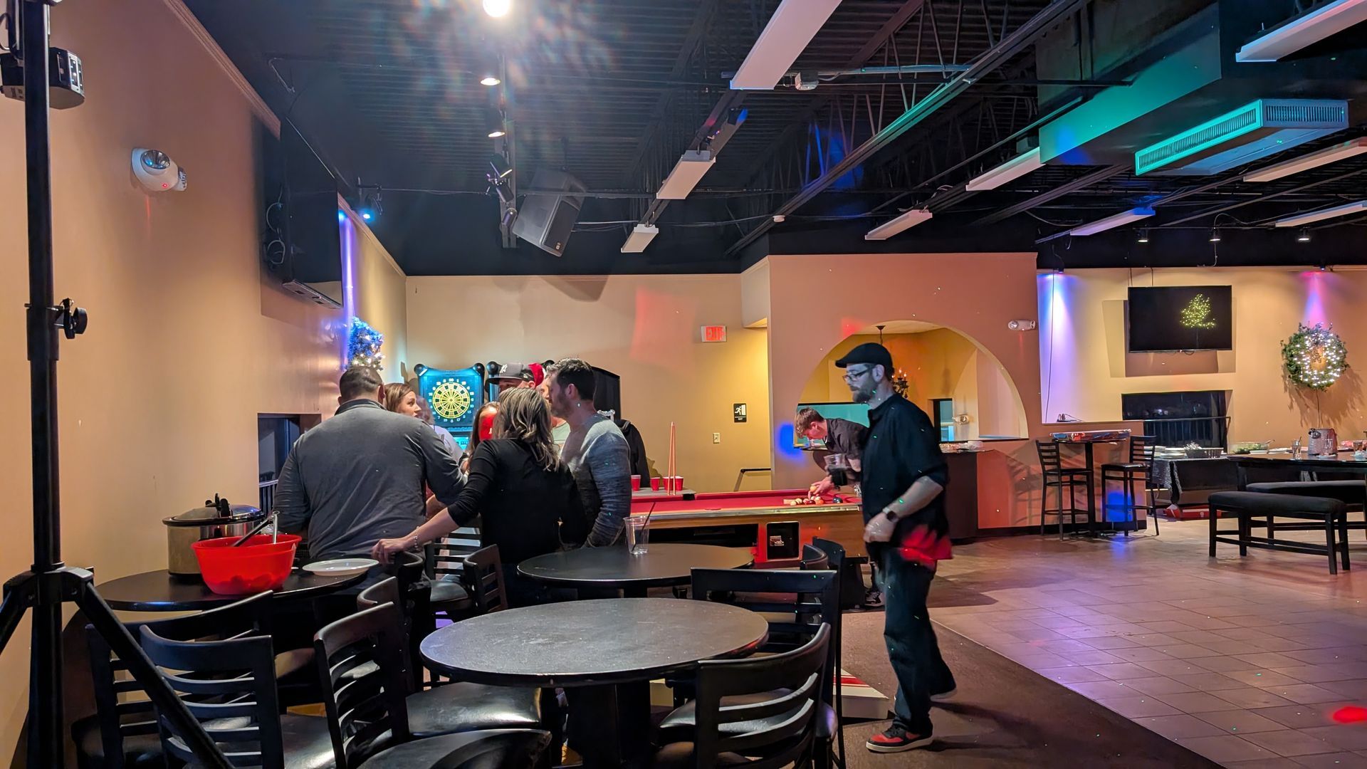 Dim bowling alley with people at lanes, tables, and neon lights in the background