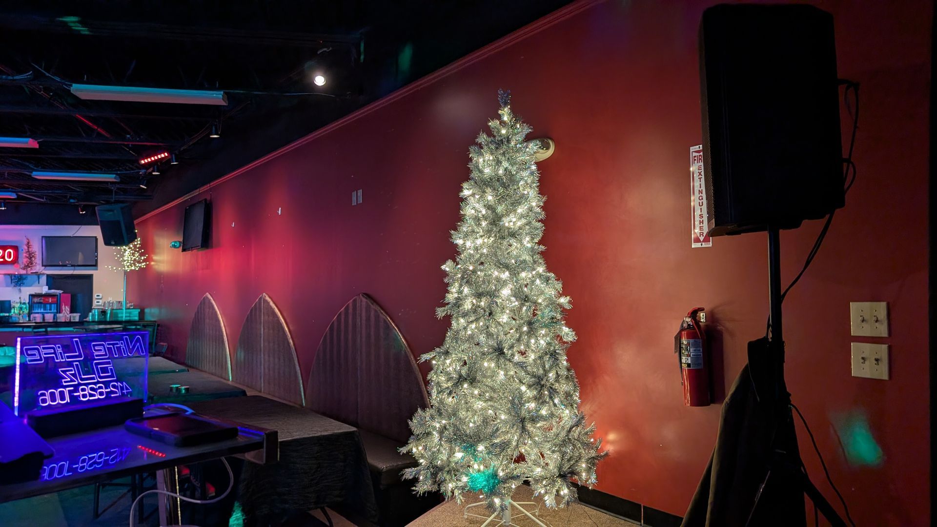 Dimly lit room with a white Christmas tree beside a red wall and black speaker.