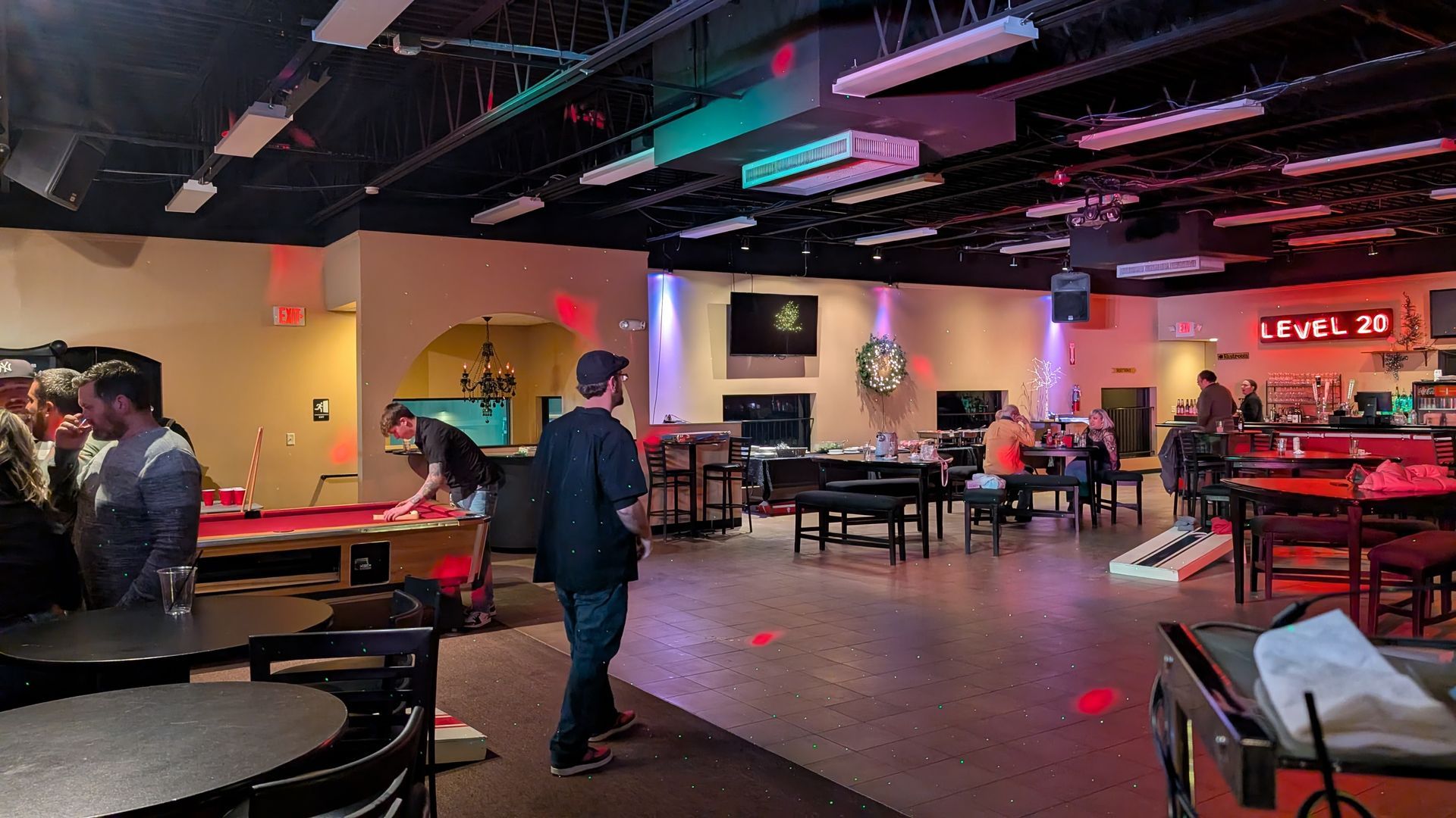 Dim arcade/bar with neon lights, pool tables, and a few people milling around.