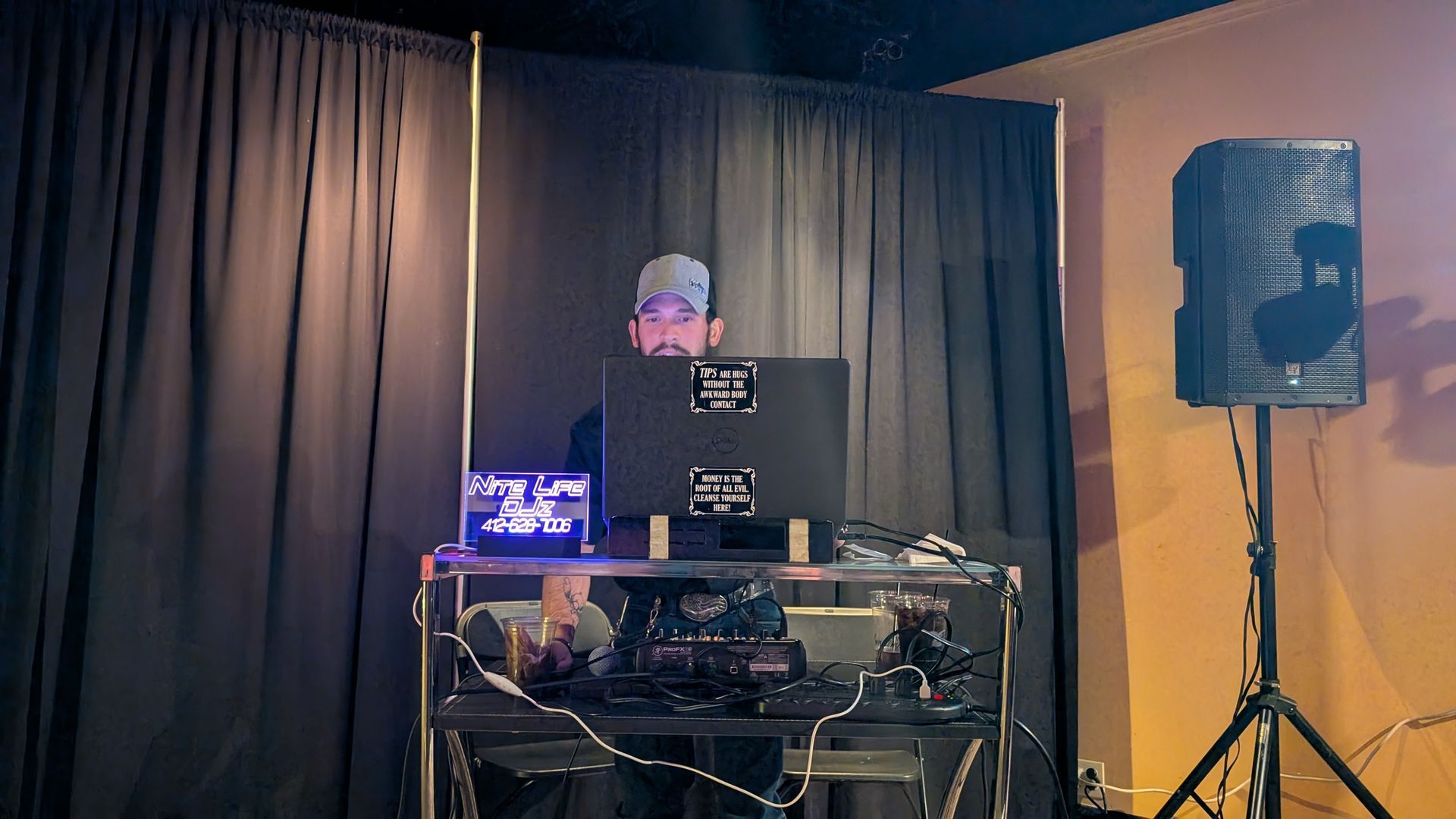DJ at a mixing booth on stage with black curtains and a large speaker on the right