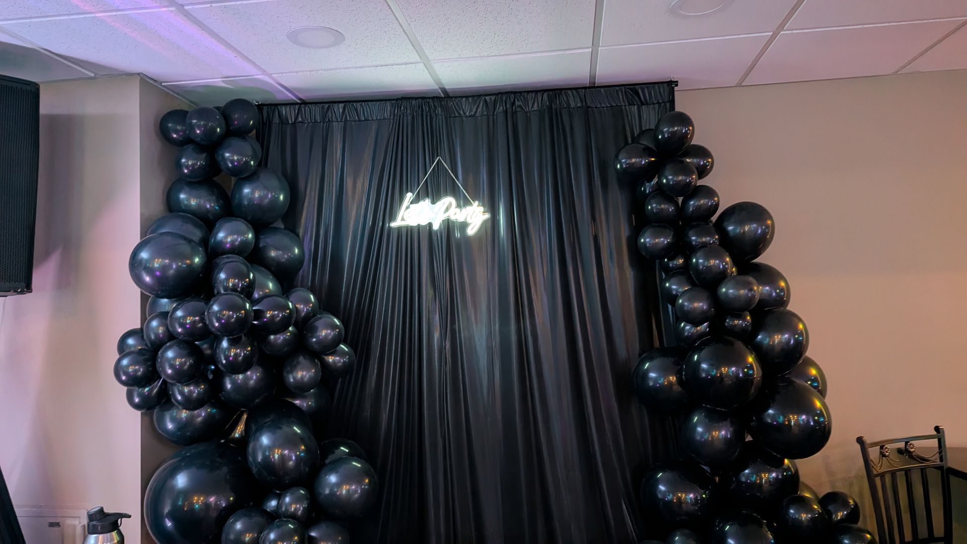 Black balloon arch framing a shiny black curtain backdrop with a chandelier in an indoor event space