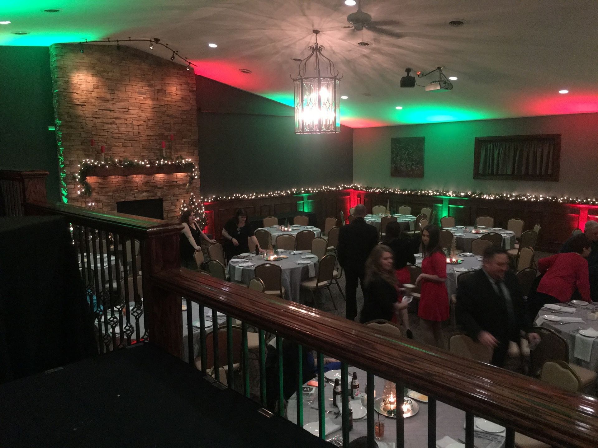 Dimly lit banquet hall with red and green lights, stone fireplace, and guests seated at tables.