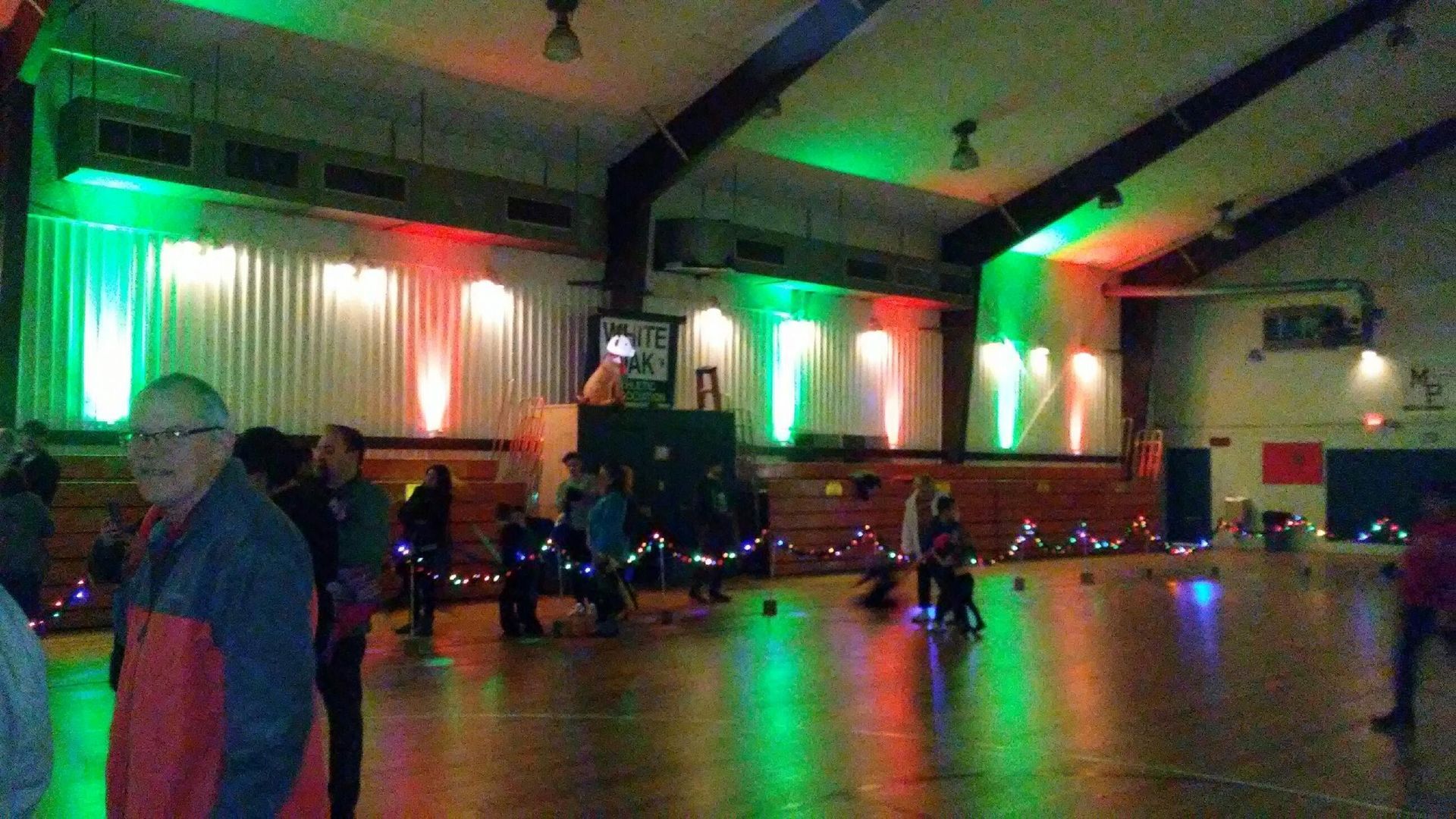 Dimly lit indoor roller rink with people skating under red and green lights