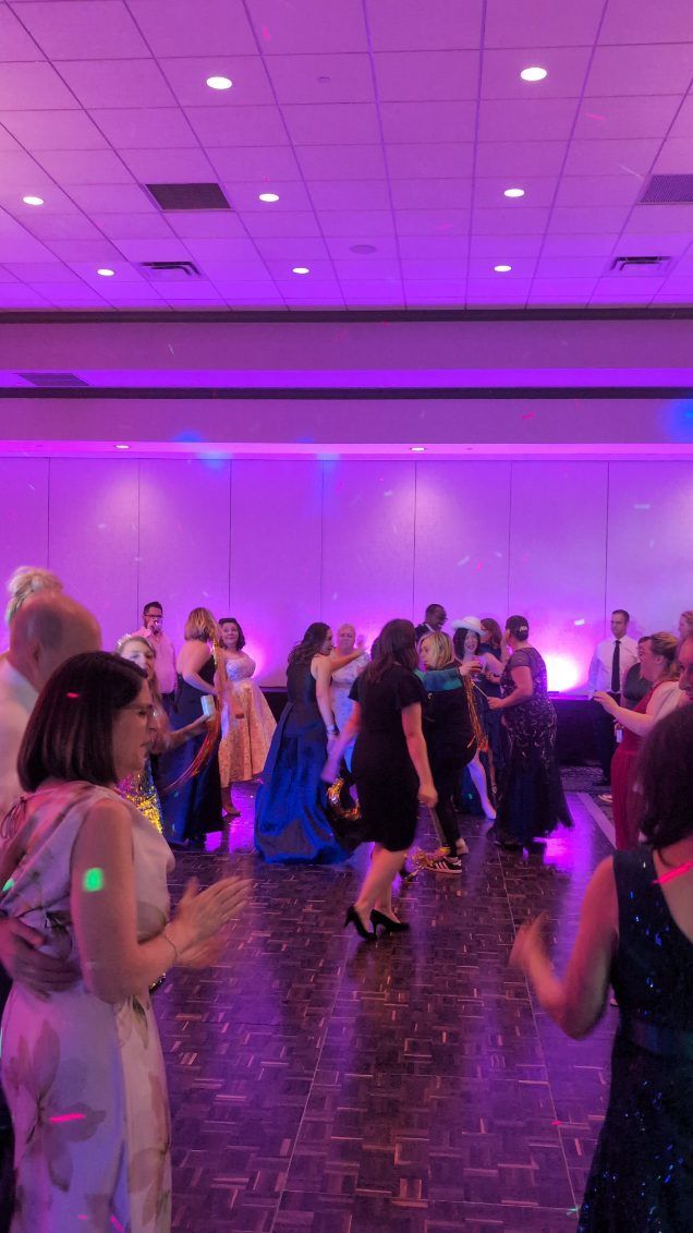 People dancing at a purple-lit indoor party or event with a crowd and tiled floor.