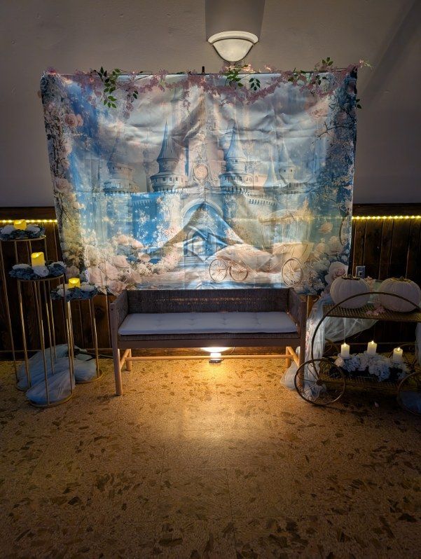 Decorated memorial display with a blue-white backdrop, flowers, bench, and candles in a dim room