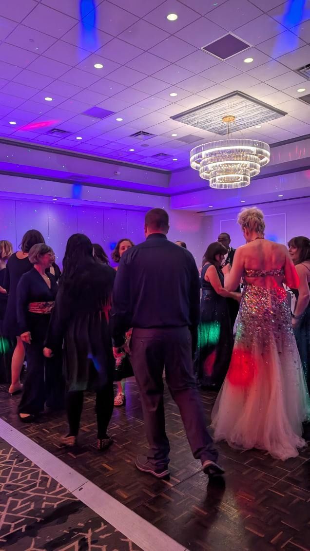 Guests dancing at a purple-lit banquet hall with chandeliers and a woman in a pink gown in the foreground