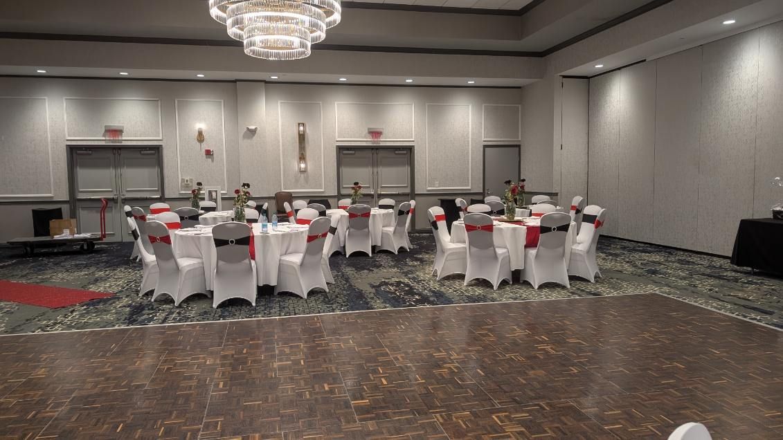 Formal banquet hall with round tables, white chair covers, and red napkins beneath chandeliers