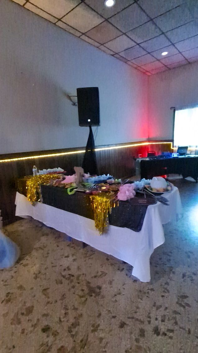 Decorated buffet table with white cloth, gold tinsel, flowers, and a speaker in a hall