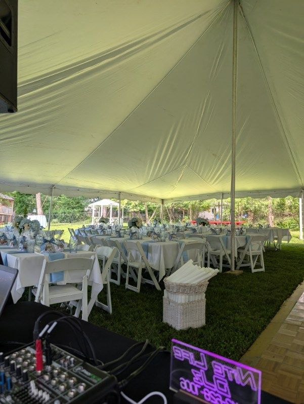 White event tent with round tables and chairs on grass, with DJ equipment in the foreground