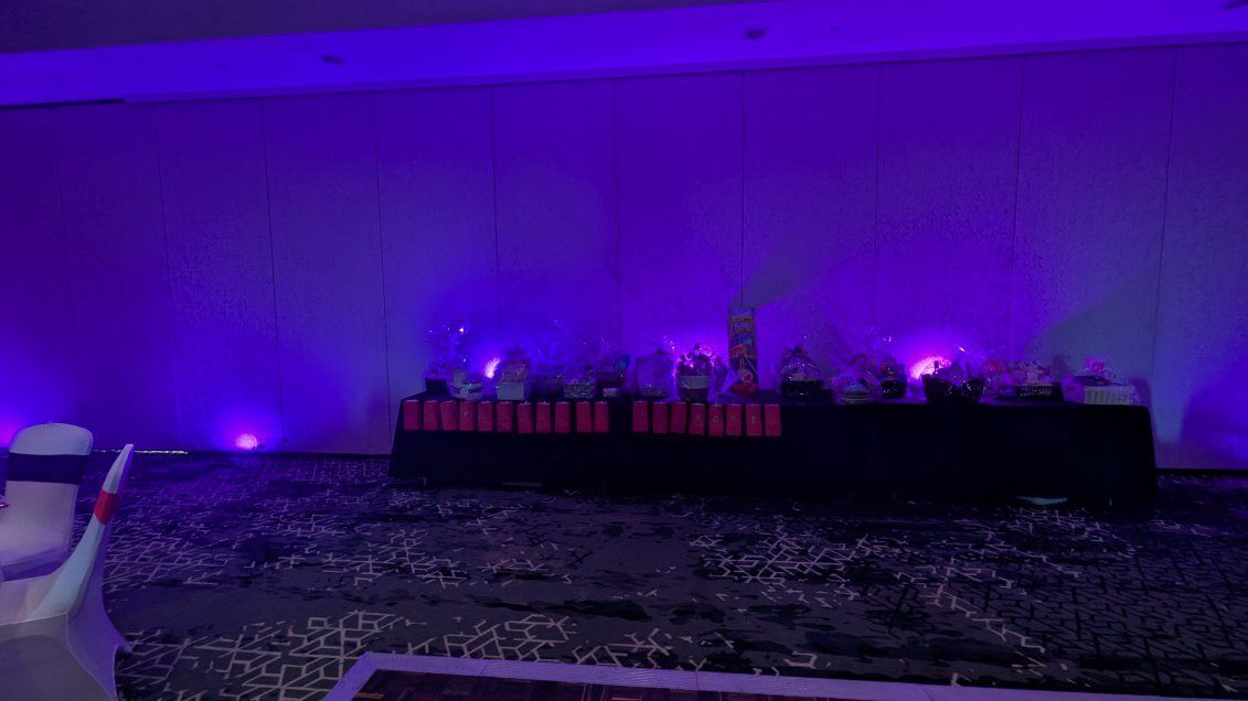 Purple-lit display of a long table with miniature buildings and small lights in a dark room