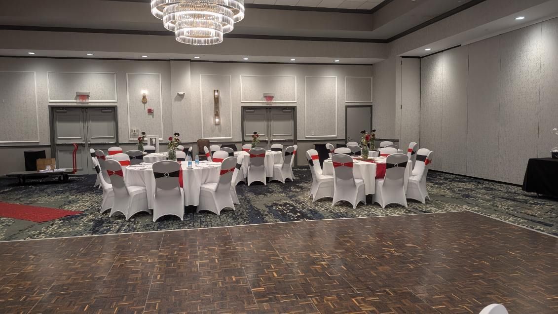 Empty banquet hall with round tables and white chair covers, set for an event under chandeliers