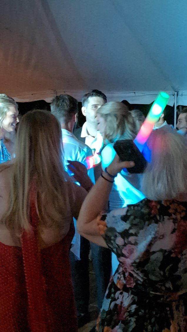 Crowd dancing at a party, with colorful glow sticks and dim tent lighting