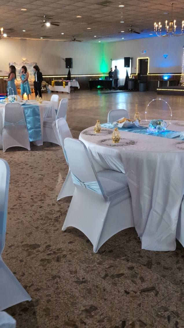 Round banquet hall with white-draped tables, chairs, and blue-green uplighting along the back wall.