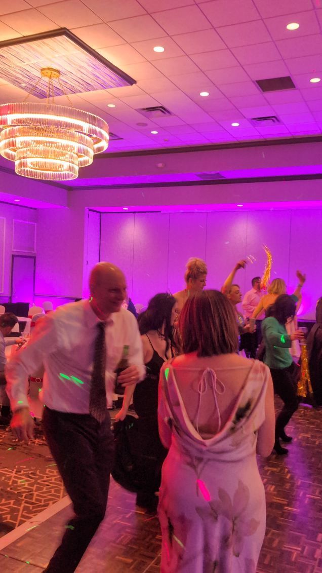 People dancing at a purple-lit party in a ballroom with a chandelier