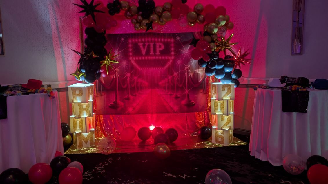 Pink VIP party backdrop with flowers, lights, balloons, and draped tables on either side