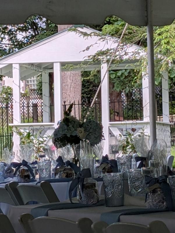 White tented outdoor reception with tables, wrapped chairs, and floral centerpieces in a garden setting