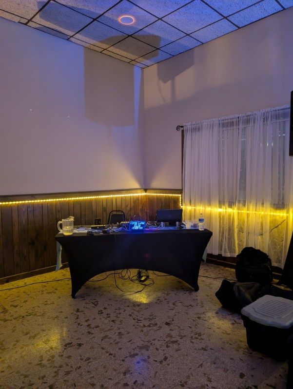 Dim room with a black-draped DJ table, yellow accent lights, and a curtain backdrop on the right.