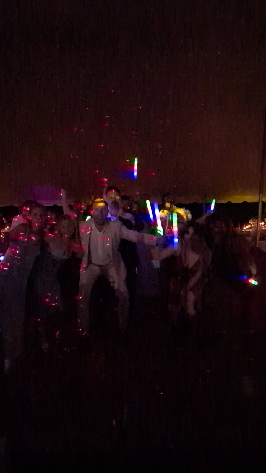 Crowd at a dark concert waving colorful glow sticks under bright lights