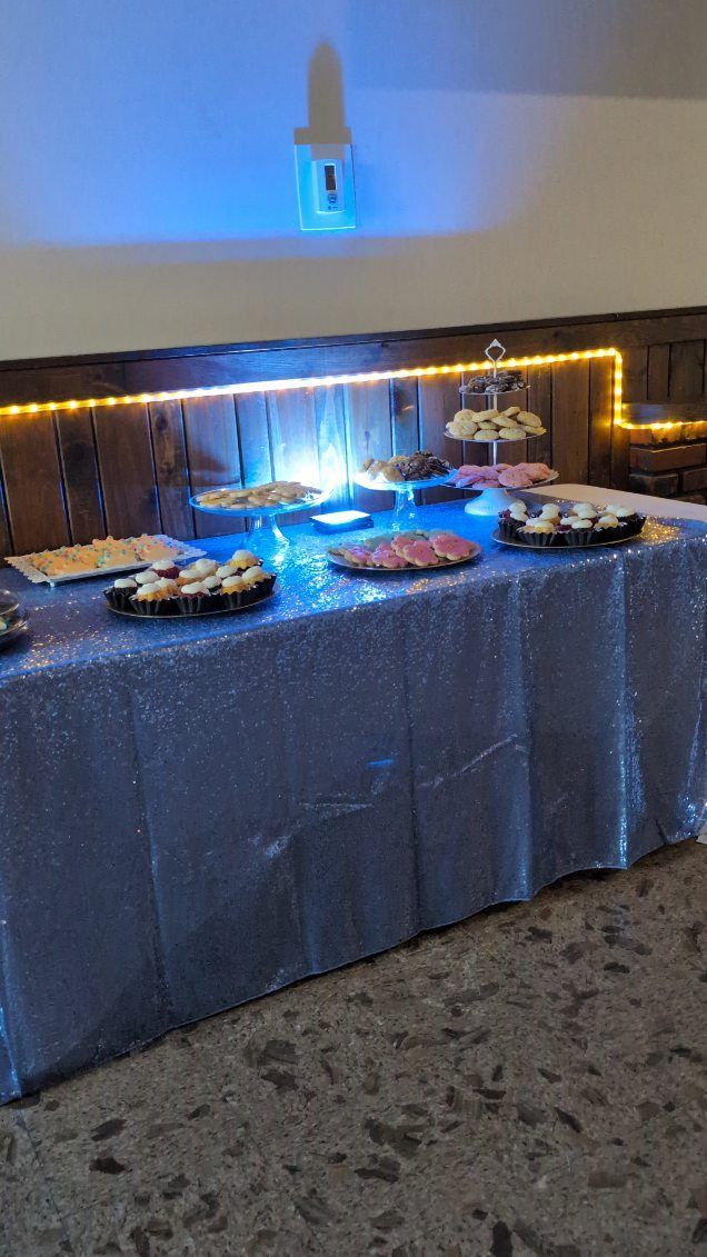 Blue-lit buffet table with trays of food and a silver sequin tablecloth in a banquet room