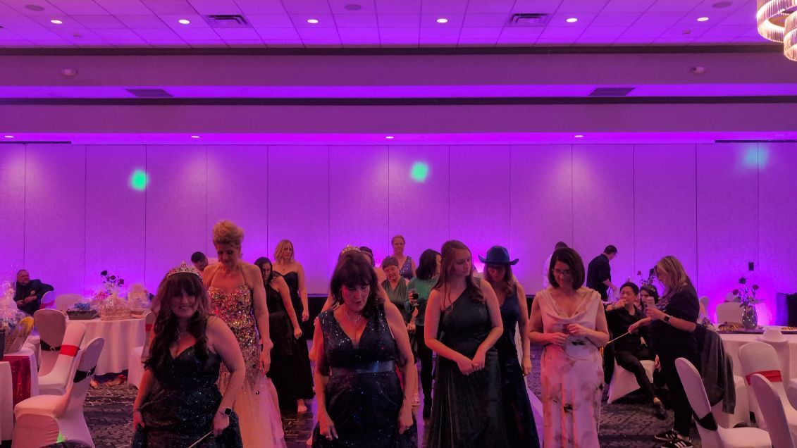 Guests dancing in a purple-lit banquet hall with round tables and formal decor
