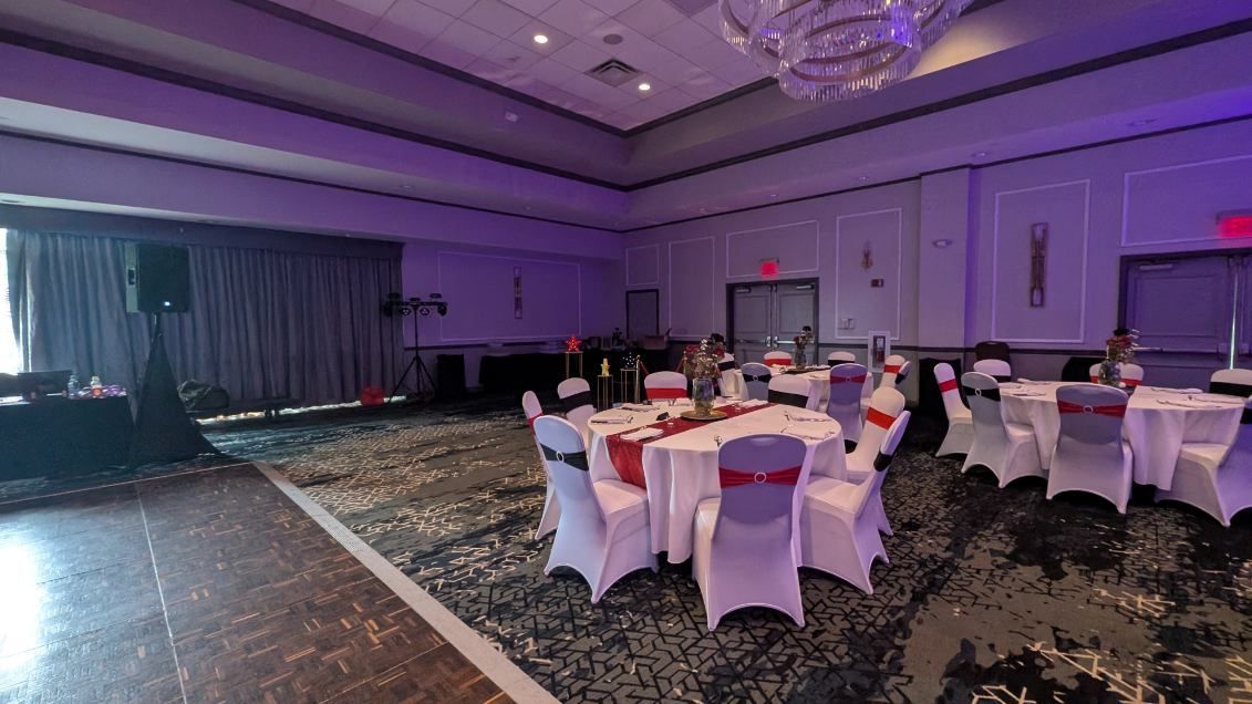 Purple-lit banquet hall with round tables, white chair covers, and a stage at the front