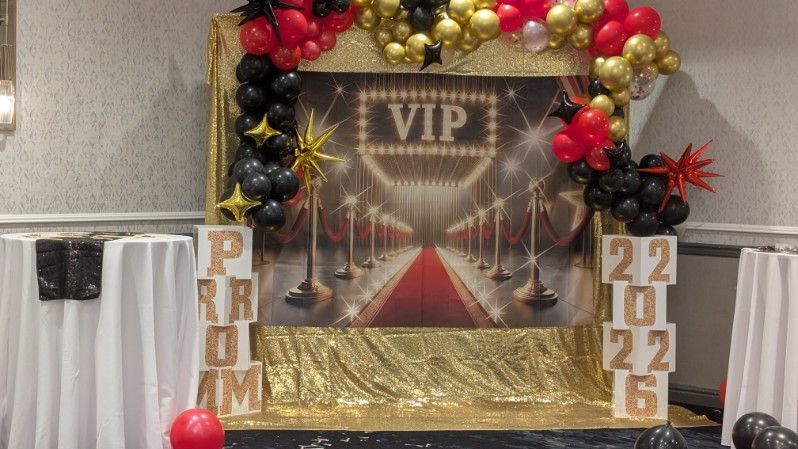 VIP backdrop with gold-and-red balloon arch, red carpet, and gold 2022 pillars in a decorated room
