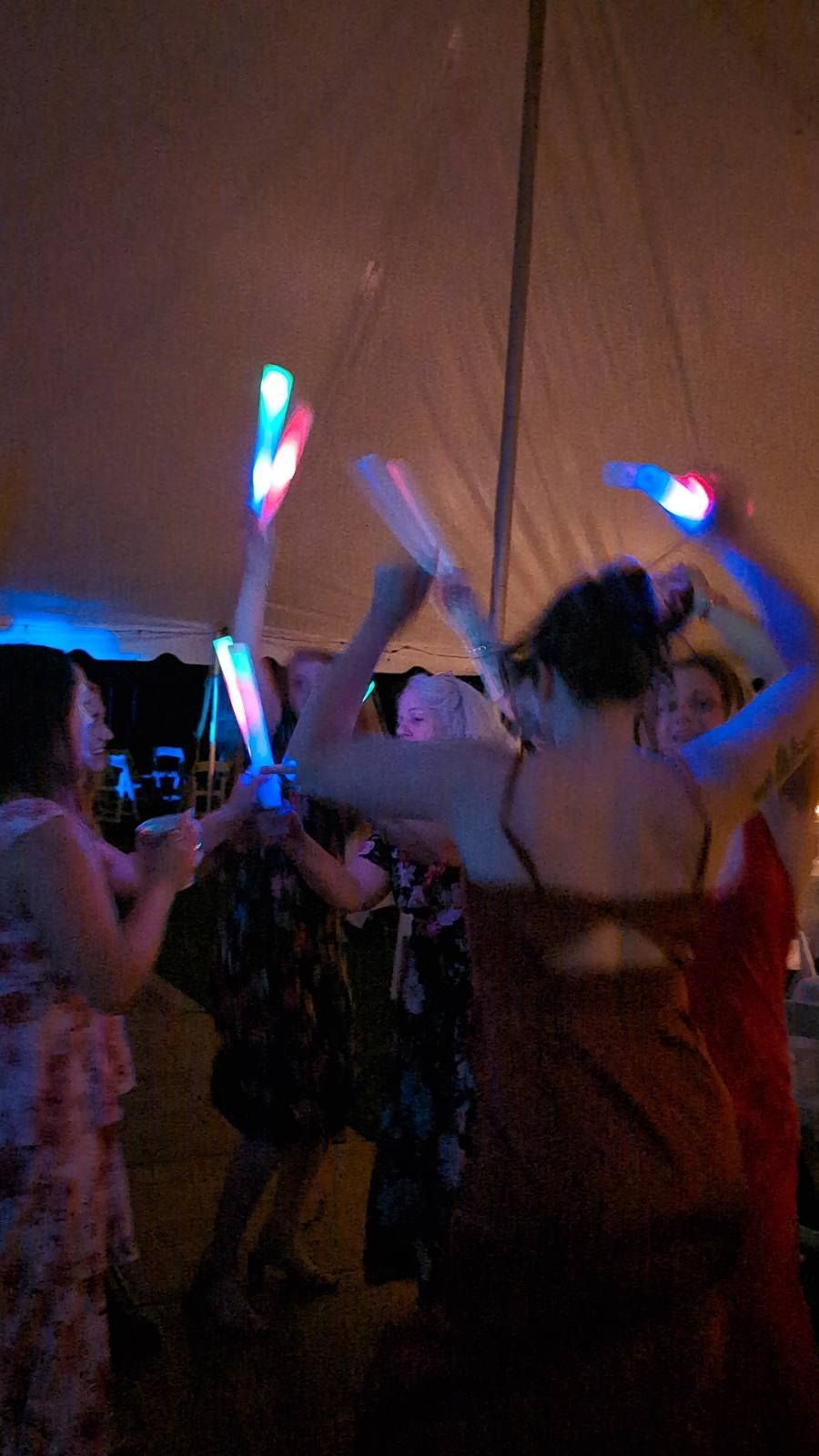 People dancing in a dim tent, waving colorful glow sticks at a party or concert.