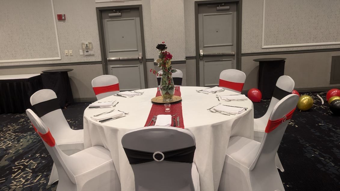 Round banquet table with white chair covers and red accents in a decorated event room