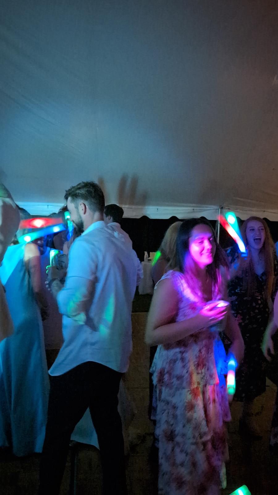 People dancing at a party under blue and pink lights, one holding a glowing cup.