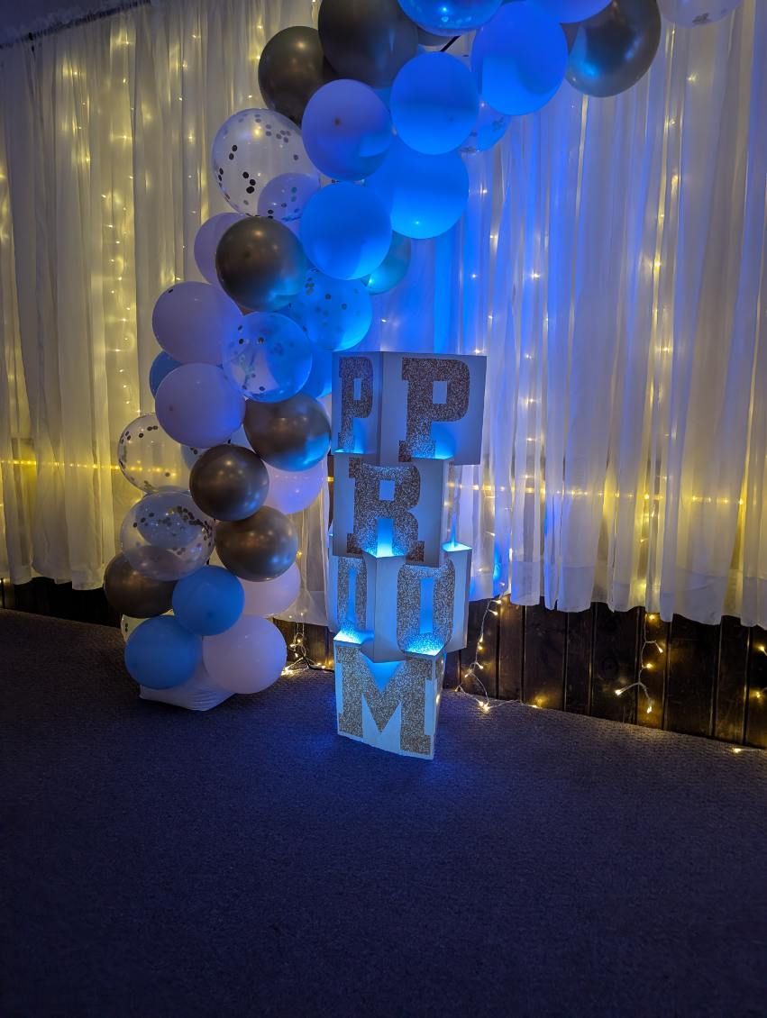 Blue and silver balloon column beside illuminated letter blocks at an event backdrop