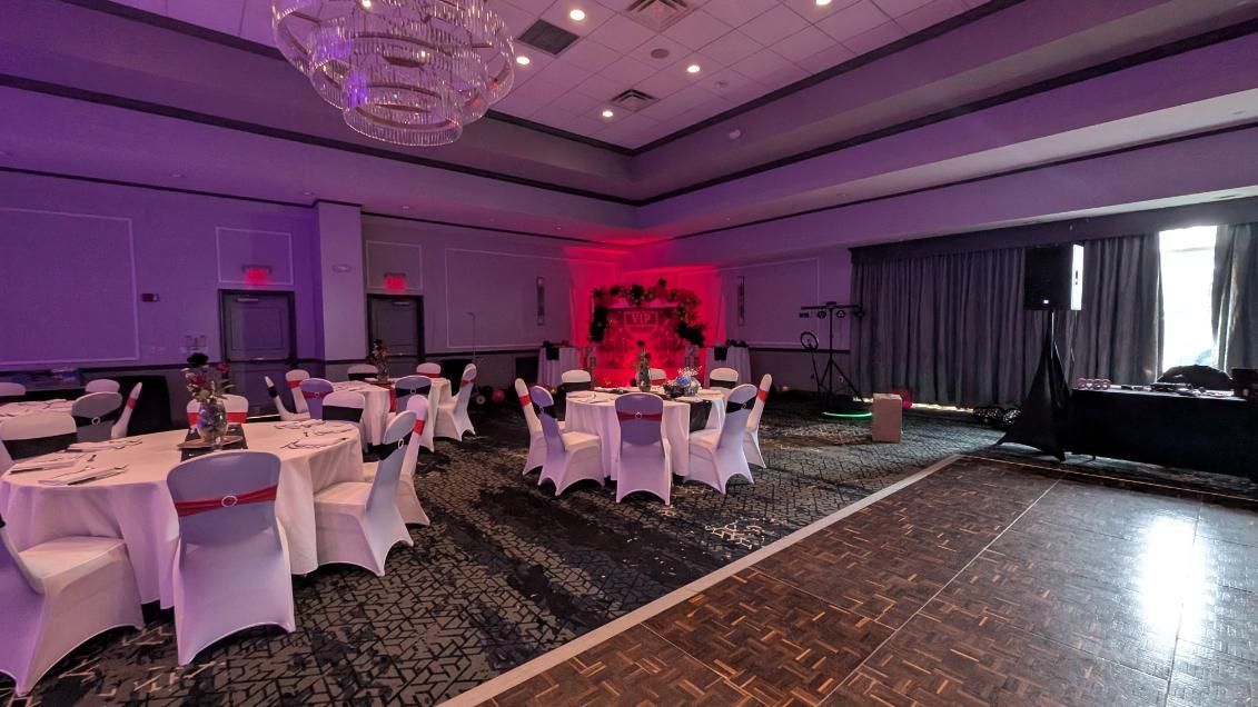 Elegant banquet hall with round white-clothed tables, chandeliers, and a red-lit stage area