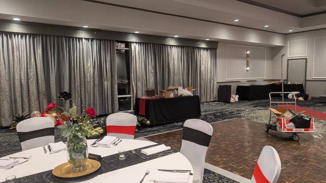 Conference room with round tables, white chairs with red sashes, long draped wall, and a buffet table at the back