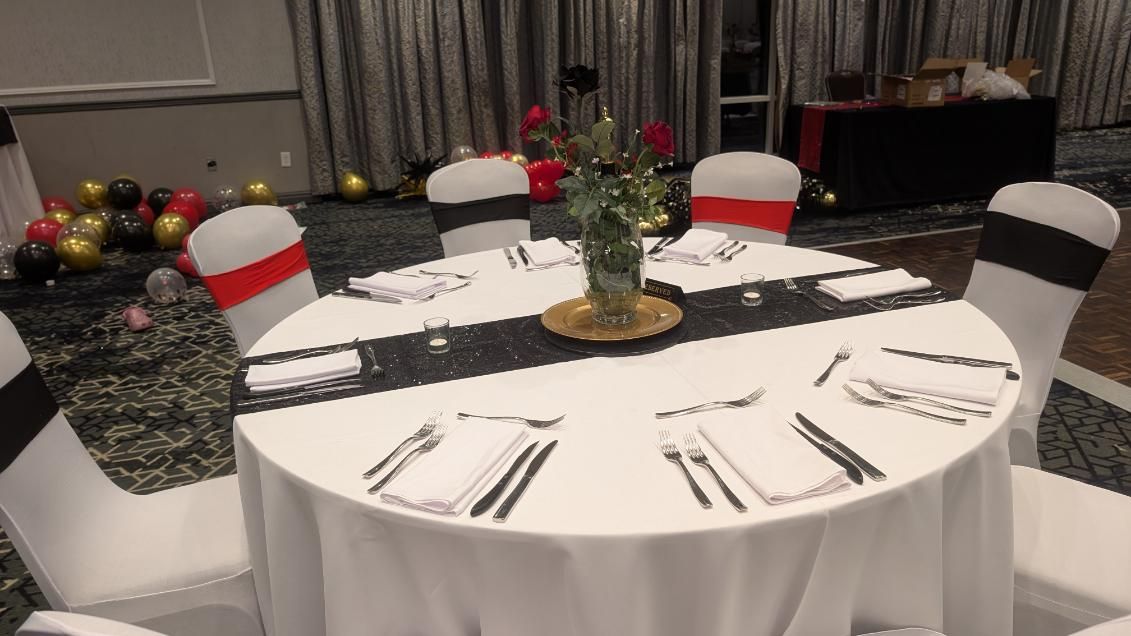Round banquet table with white cloth, black runner, red-and-white chairs, and place settings in a decorated room