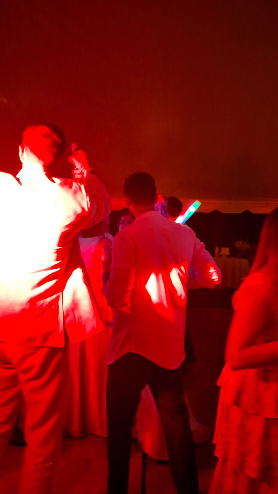 People dancing at a red-lit party, one holding a glowing light stick.