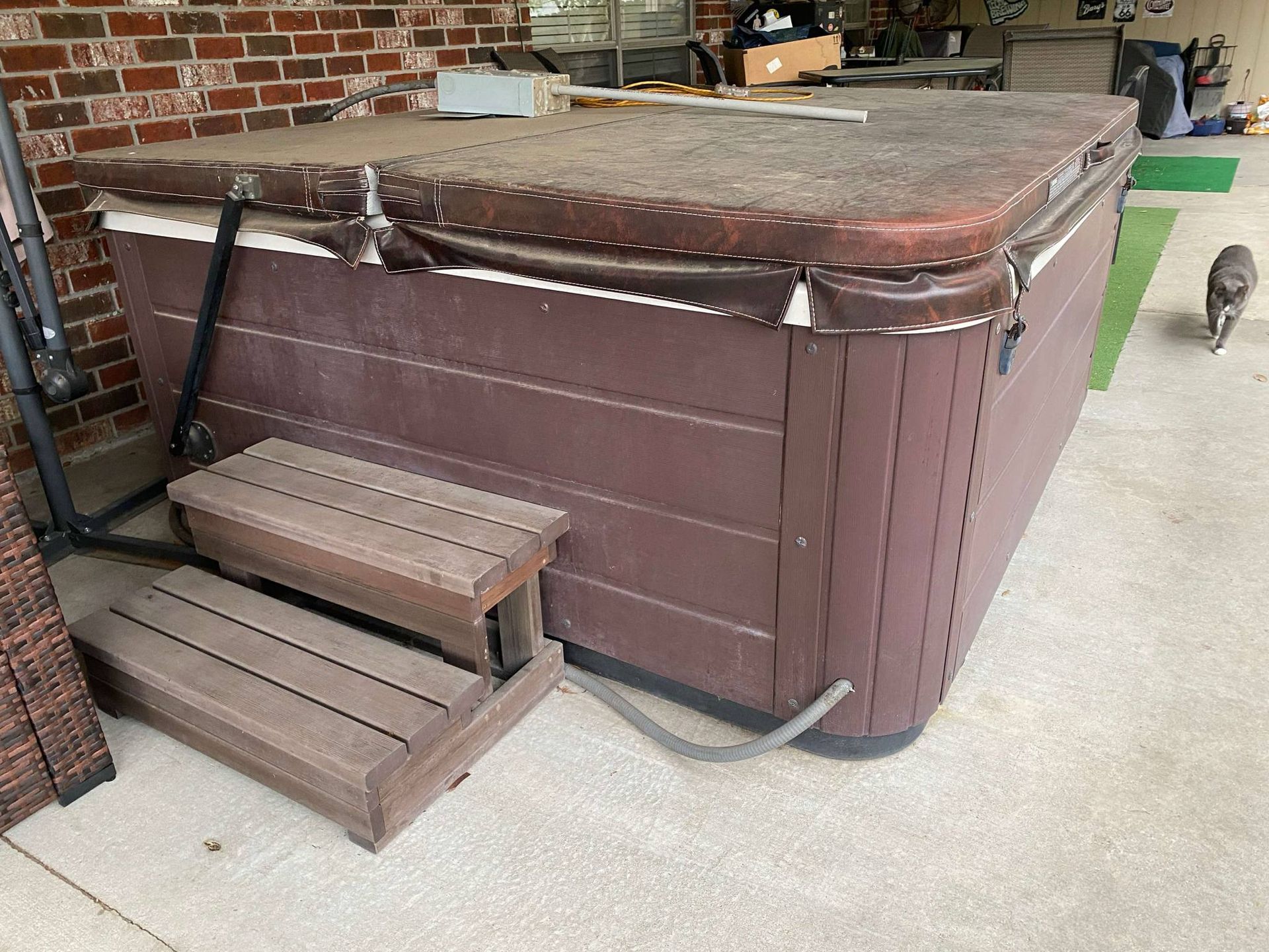 A brown hot tub with wooden steps is sitting on a patio.