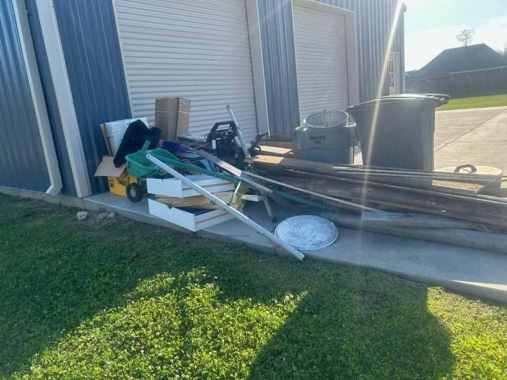 A pile of junk is sitting on the sidewalk in front of a garage.