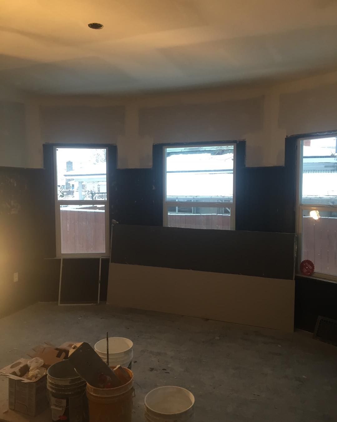 A room with three windows and buckets of paint on the floor