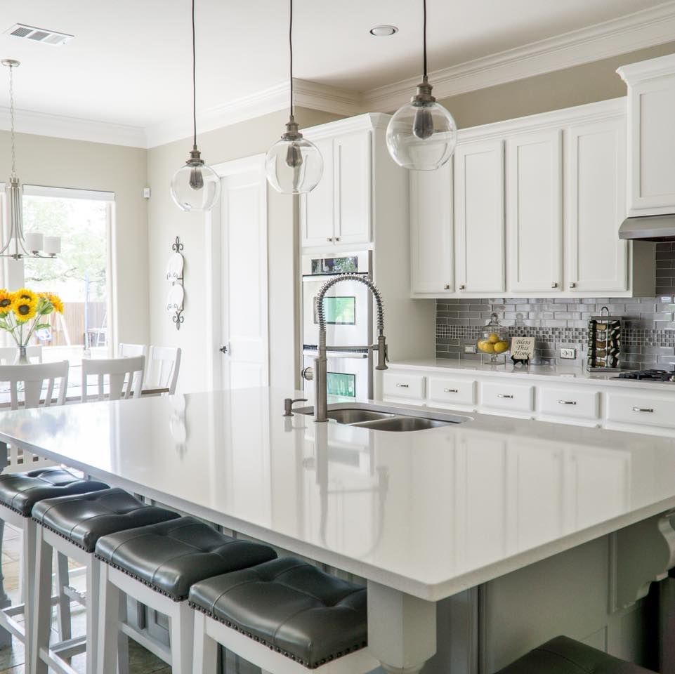 A kitchen with white cabinets and a large island with stools
