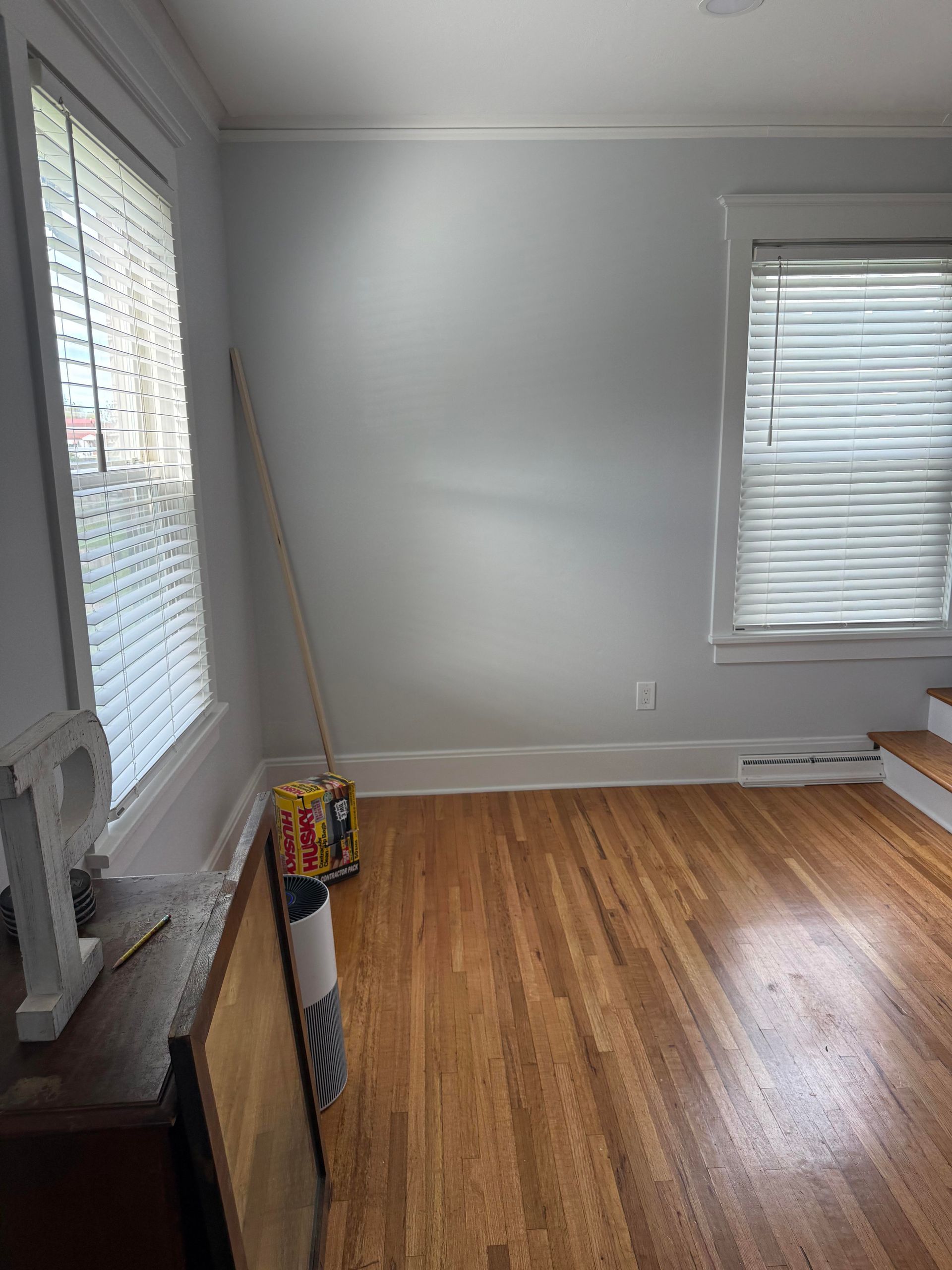 Empty room with gray walls, hardwood floor, and two windows with blinds.