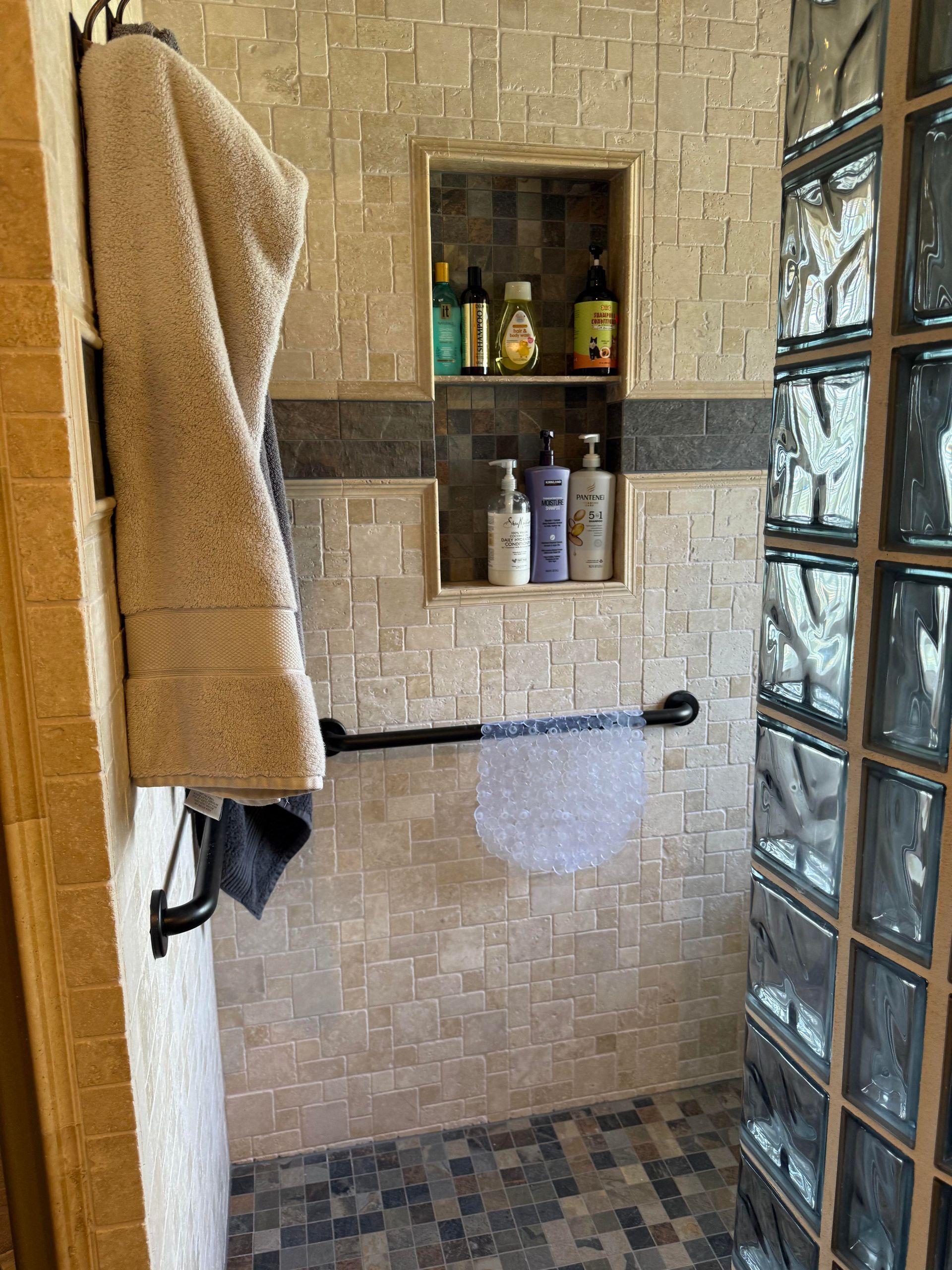 Tiled shower with tan towels, glass block wall, and built-in shelves of toiletries