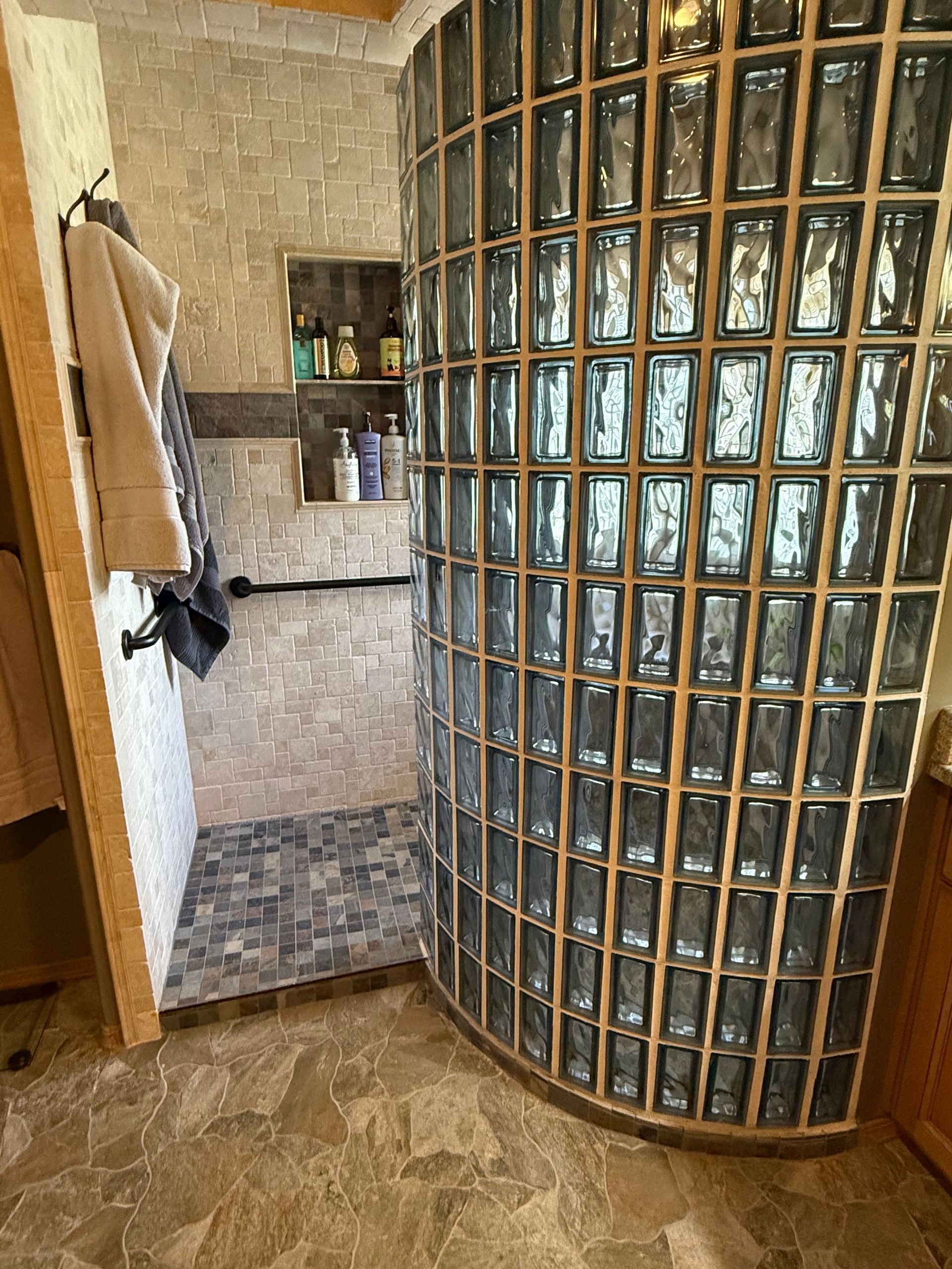 Curved glass block shower wall beside a tiled bathroom nook and wooden door frame.